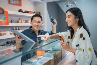 Kadın müşteri, erkek vape satıcısının elinde bulunan dijital tableti işaret ediyor.