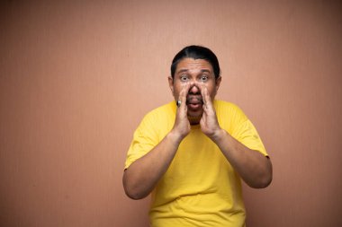 Sarı tişört giyen yaşlı Asyalı adam arka planda fısıldayan hareketlerle sırlarını anlatıyor.