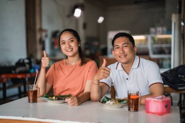 Asyalı çift, pekel yemek standında birlikte yemek yerken başparmak kaldırıyor.