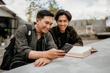 İki öğrenci cep telefonlarını kullanarak dışarıda bir kafede oturup kitap okuyor.