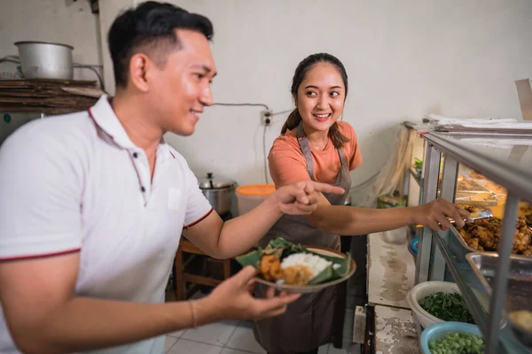 男性の顧客は伝統的な屋台で女性のウエイトレスと指を指して食べ物を選ぶ — ストック写真