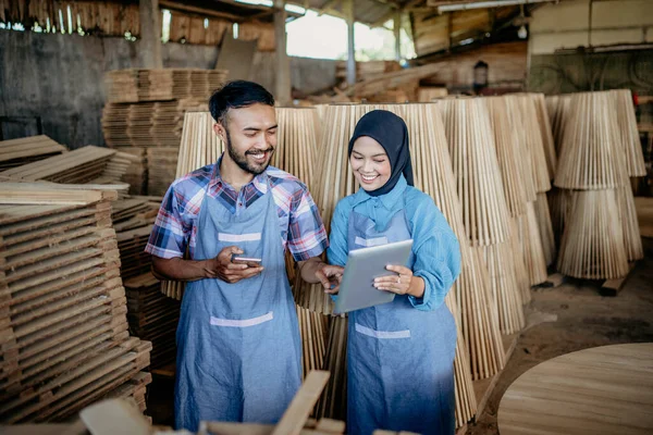 ヒジャーブ州の男性と女性の起業家は 木製の店で携帯電話を保持しながら一緒にタブレットを使用します — ストック写真