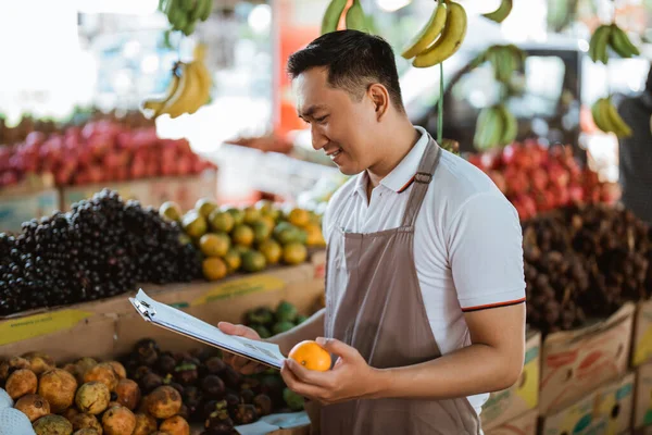 Férfi Eladó Kötényben Tartja Mandarin Gyümölcsöt Ellenőrzi Gyümölcslistát Vágólapon — Stock Fotó