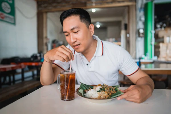 英俊潇洒的亚洲男人一边喝茶一边用稻草 一边在山核桃摊的饭桌边吃午饭 — 图库照片