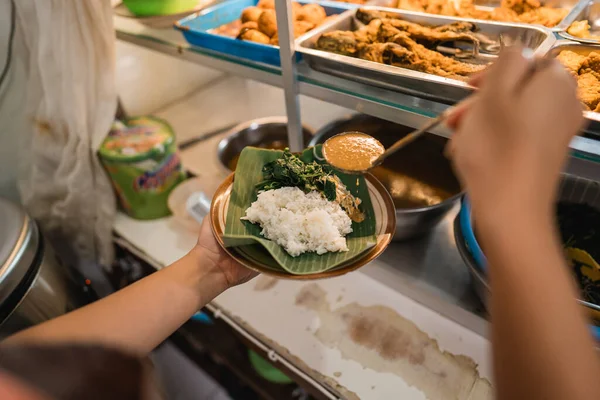 一只手拿着一盘米饭和蔬菜的特写镜头 同时用木勺在传统的食品店里拿起花生酱 — 图库照片