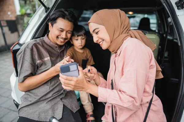 快乐的亚洲穆斯林家庭与孩子坐在汽车后备箱与手提箱准备为埃德穆巴拉克假期的公路之旅 — 图库照片