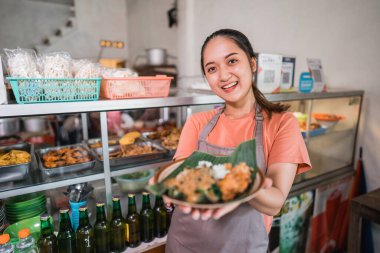 Çekici Asyalı kız yemek standında bir tabak pekel yemeği gösteriyor.