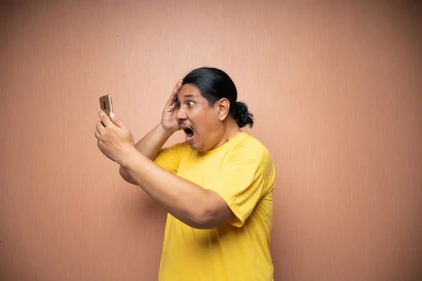 亚洲的老人穿着黄色的T恤 手持手机 用手机在平平的背景下相互发短信或视频通话 — 图库照片