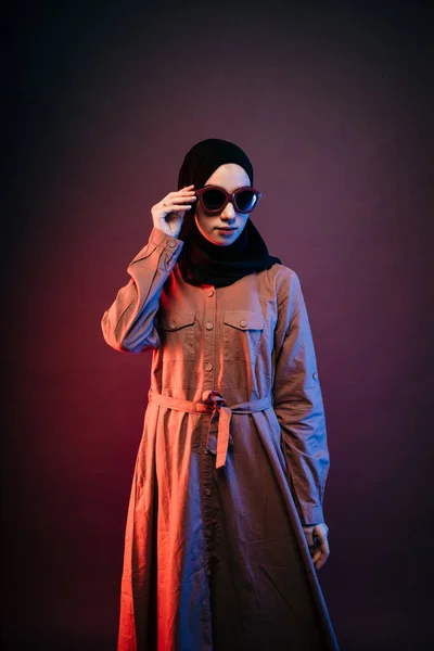 穆斯林妇女身穿黑色头巾橙色长裙 手持太阳镜 侧看镜头 摆出一副相机的姿势 — 图库照片