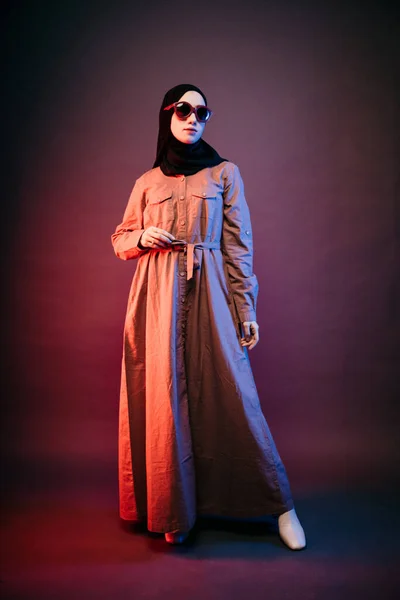 穆斯林妇女戴着黑色头巾橙色长裙太阳镜 向侧面看了看 弯了弯手 — 图库照片