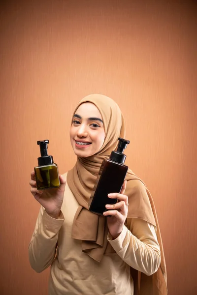 身穿头巾和奶油T恤衫的穆斯林妇女拿着护身瓶在橙色背景下对着摄像机微笑 — 图库照片