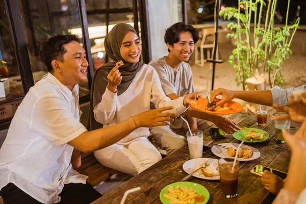 身穿头巾的年轻亚洲女人在户外咖啡馆里一边吃东西一边给朋友们端盘子里的食物 — 图库照片