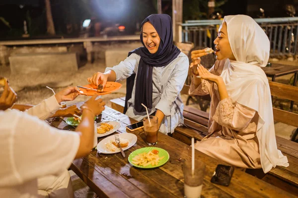 ヒジャーブのアジア人女性は屋外カフェでIftar中に友人のプレートから食べ物を取ります — ストック写真