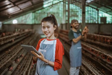 Tavuk çiftliğinde erkek işçilerin yumurtaları kontrol ettiği tablet kullanan mutlu kadın işçiler.