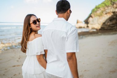 Beyaz elbiseli şirin genç bir çift sahilde birlikte geziyorlar.