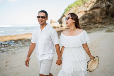 Mutlu genç Asyalı çift sabahları kumsalda el ele yürür.