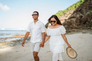 Yakışıklı bir adam ve güzel bir kadın sahilde yürürken el ele tutuşuyorlar.