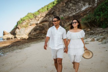 Beyaz elbiseli genç çift, sabahları sahilde egzotik deniz kenarında el ele dolaşırlar.