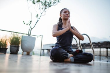 Kadın, havuzun kenarında oturmuş meditasyon hareketleriyle yoga yapıyor.