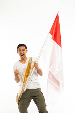 Beyaz tişörtlü yakışıklı Asyalı bir adam ve omuz kemeri gibi duran bir sarong üzerinde Endonezya bayrağı olan bir sopa getirin ve kolunu sıkın.