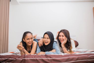 Üç kadın yatak odasında yatakta yatarken gülüyor.