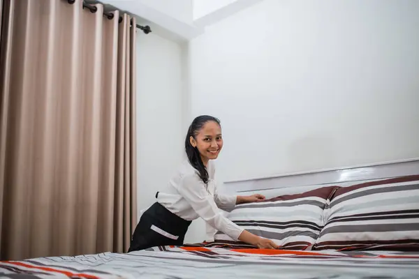 Asian woman smiling hotel maid smoothing a pillow on a bed in a hotel room