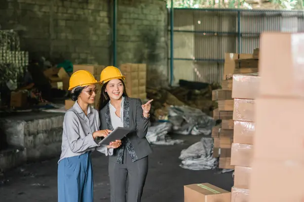 two Asian women factory employees checking and pointing at goods in the warehouse
