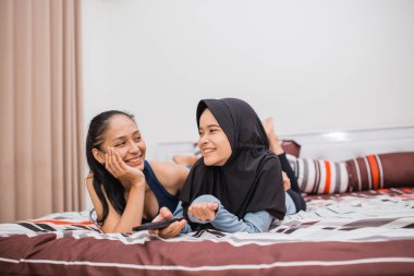 İki kadın, yatakta televizyon izlerken kumandayı tutarak rahatladı.