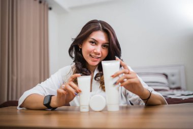 Çekici bir kadın, elinde tüp paketleri tutarken gülümsüyor. Oda arkası kozmetik ürünü gibi.