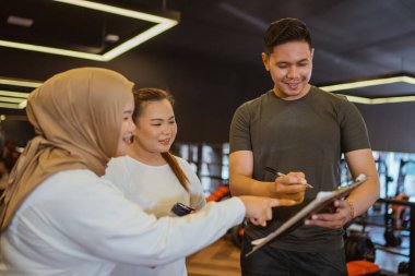 Erkek eğitmen spor salonundaki stajyeri için antrenman planını açıklıyor.