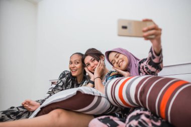 Yatakta otururken cep telefonu kullanan üç en iyi arkadaş selfie 'si.