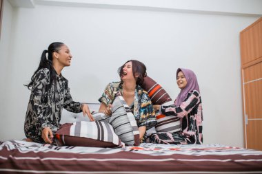 Pijamalı üç kız yatakta şakalaşırken gülüyorlar.