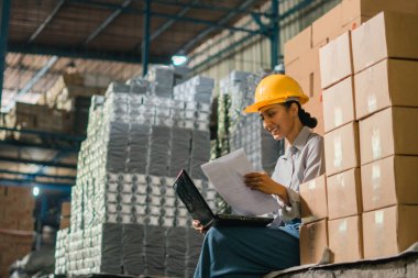 Bayan fabrika işçisi fabrikada çalışırken dizüstü bilgisayar kullanarak oturur.