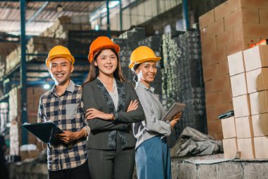 gülümseyen Asyalı iş kadınları ve şirket çalışanları bir fabrikada çapraz kolla duruyorlar.