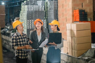 Üç Asyalı fabrika çalışanı fabrikada birlikte çalışırken sohbet ediyorlar.