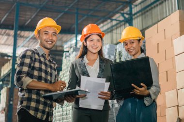 İş kadını ve müşteri kameraya gülümsüyor. Elinde kağıtlar ve fabrikada bir dizüstü bilgisayar var.