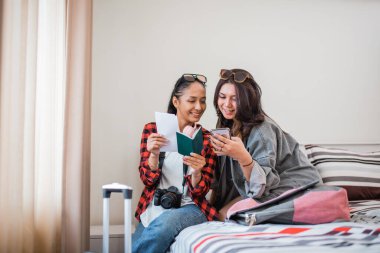 İki çekici kadın bir otel odasında oturan biletlere ve cep telefonlarına bakıyor ve kontrol ediyor.