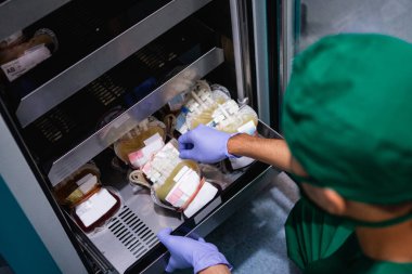 Depodaki kan torbasını çıkarırken lastik eldivenleri olan üniformalı bir doktor.