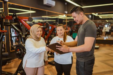Erkek eğitmen spor salonundaki stajyeri için antrenman planını açıklıyor.