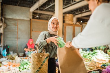 Kadın müşteriler kağıt torbaya sebze koyup alıyor ve satıcıdan yardım alıyorlar.