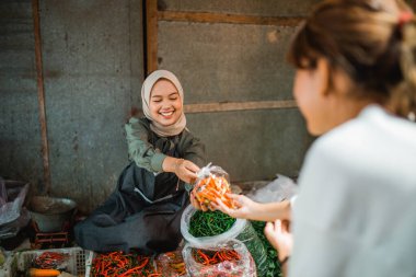 Çiftçi pazarındaki müşterisine paket sebze veren Asyalı satıcı.
