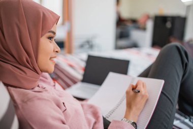 Genç tesettürlü iş kadınını kapatıyorum. Yatakta uzanmaktan zevk alırken kitap yazarak çalışıyorum.