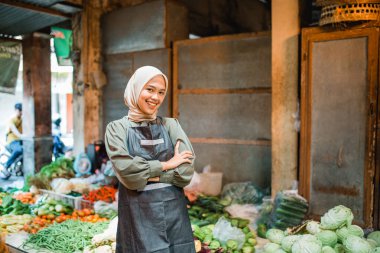 Asyalı tesettür sebze satıcısı çapraz kolla duruyor ve gülümsüyor