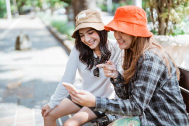 İki Asyalı kadın, bir yürüyüşten sonra oturdukları yerden turistik yerleri aramak için cep telefonu kullanıyor.
