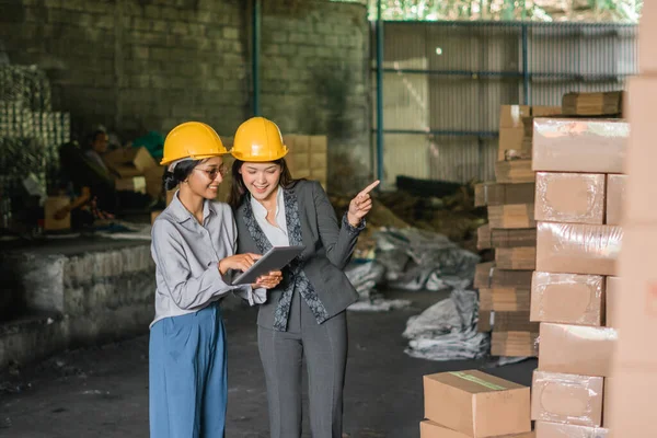 two Asian women factory employees check stock items with data using a tablet in the warehouse