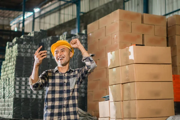 male factory worker excited while looking at cell phone while working in warehouse