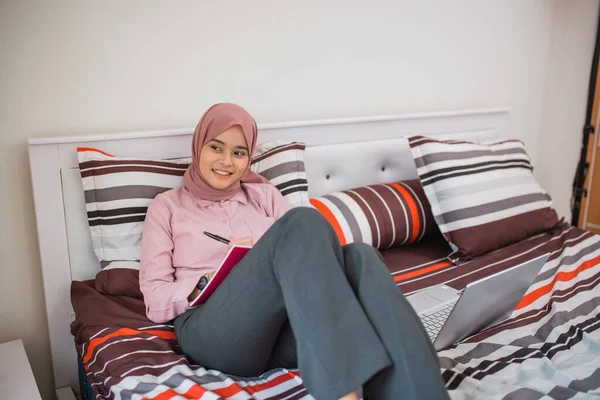businesswoman in hijab enjoys resting on the bed while working in the room