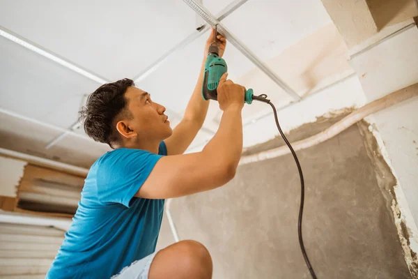 Asian young man works to install a ceiling frame with drilled bolts while renovating a roof