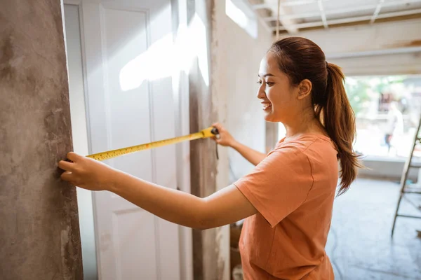 young woman measures door wicket using a tape measure while building a house