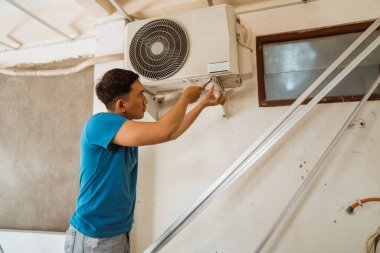 Genç Asyalı adam evde tek başına klima tamir ediyor.